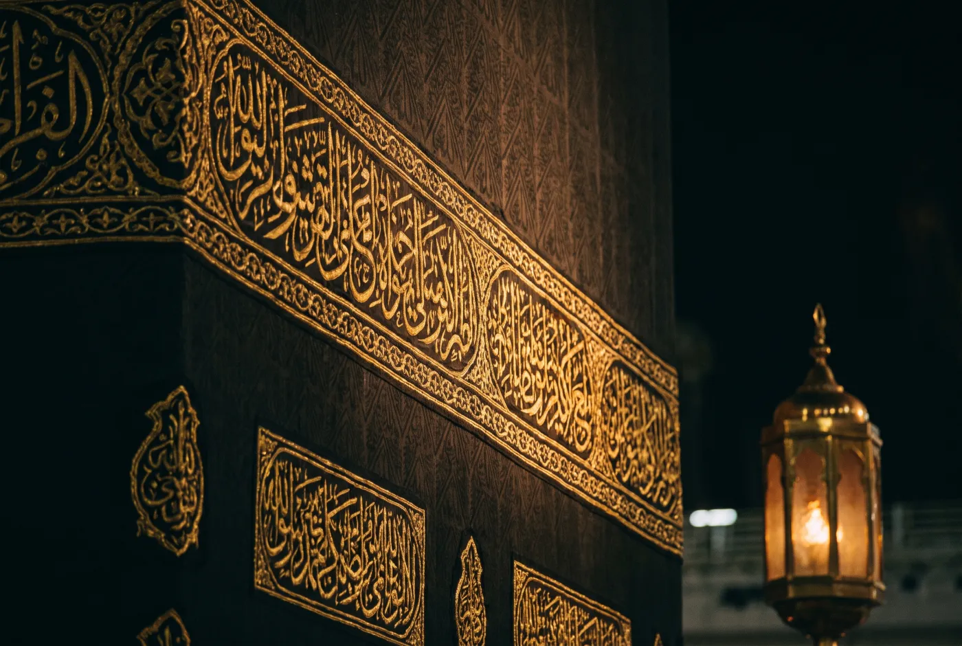 Gold-embroidered calligraphy on the Kiswa of the Kaaba, lit by a lantern
