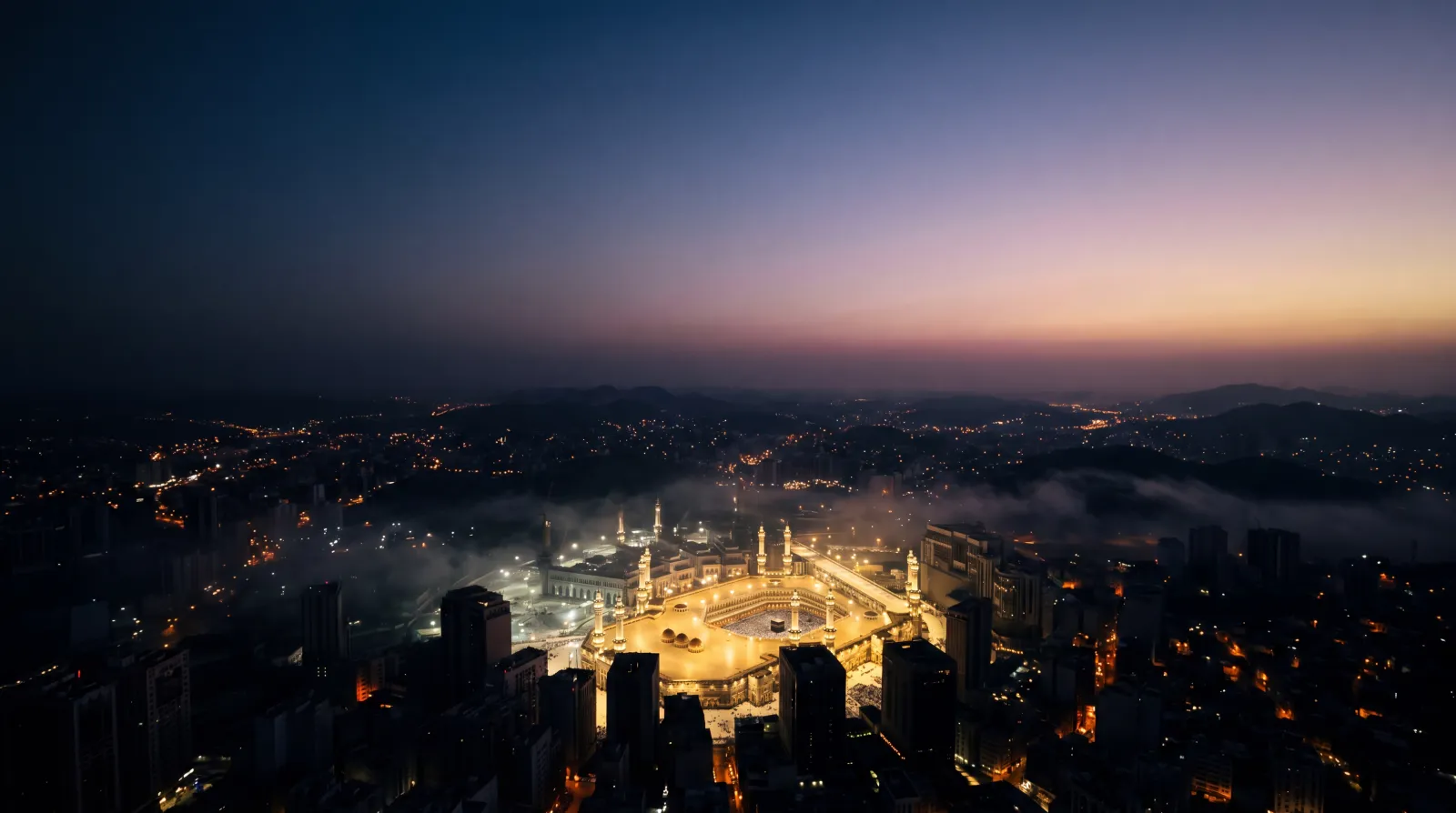 Makkah before dawn — the illuminated Grand Mosque glowing amid mist and city lights